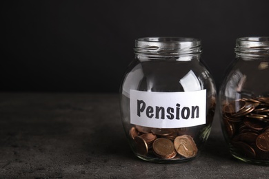 Glass jars with coins and label PENSION on dark table. Space for text