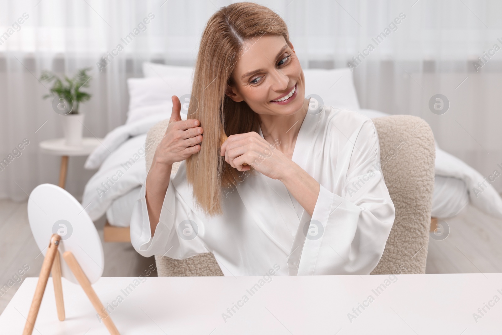 Photo of Beautiful woman brushing her hair at vanity in bedroom