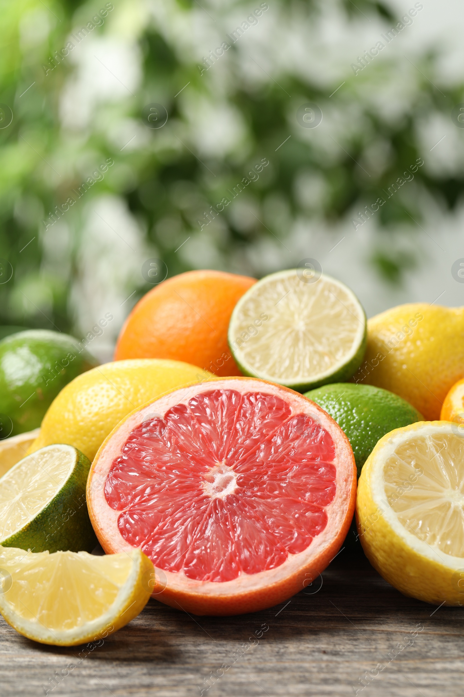 Photo of Different fresh citrus fruits and leaves on wooden table against blurred background, closeup