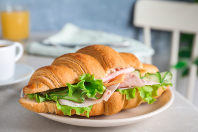 Photo of Tasty croissant sandwich with ham and cucumber on light table, closeup