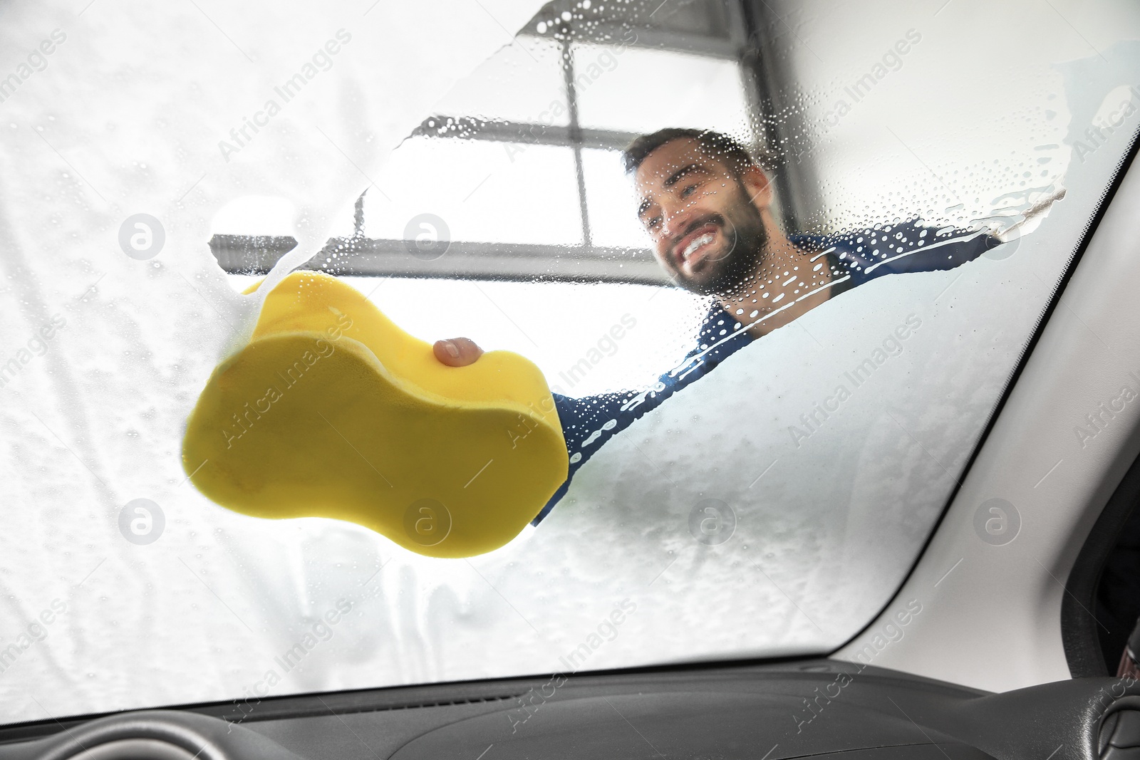 Photo of Worker cleaning automobile windshield with sponge at car wash, view from inside