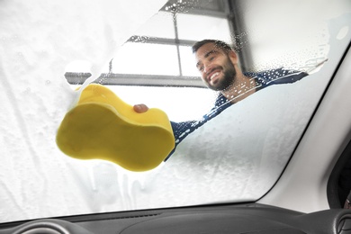 Photo of Worker cleaning automobile windshield with sponge at car wash, view from inside