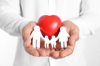 Photo of Young man holding wooden family figure and red heart on white background, closeup of hands