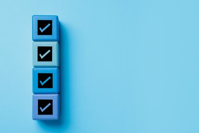 Cubes with check marks on light blue background, top view. Space for text