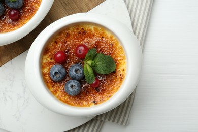 Photo of Delicious creme brulee with berries and mint in bowl on white wooden table, top view. Space for text