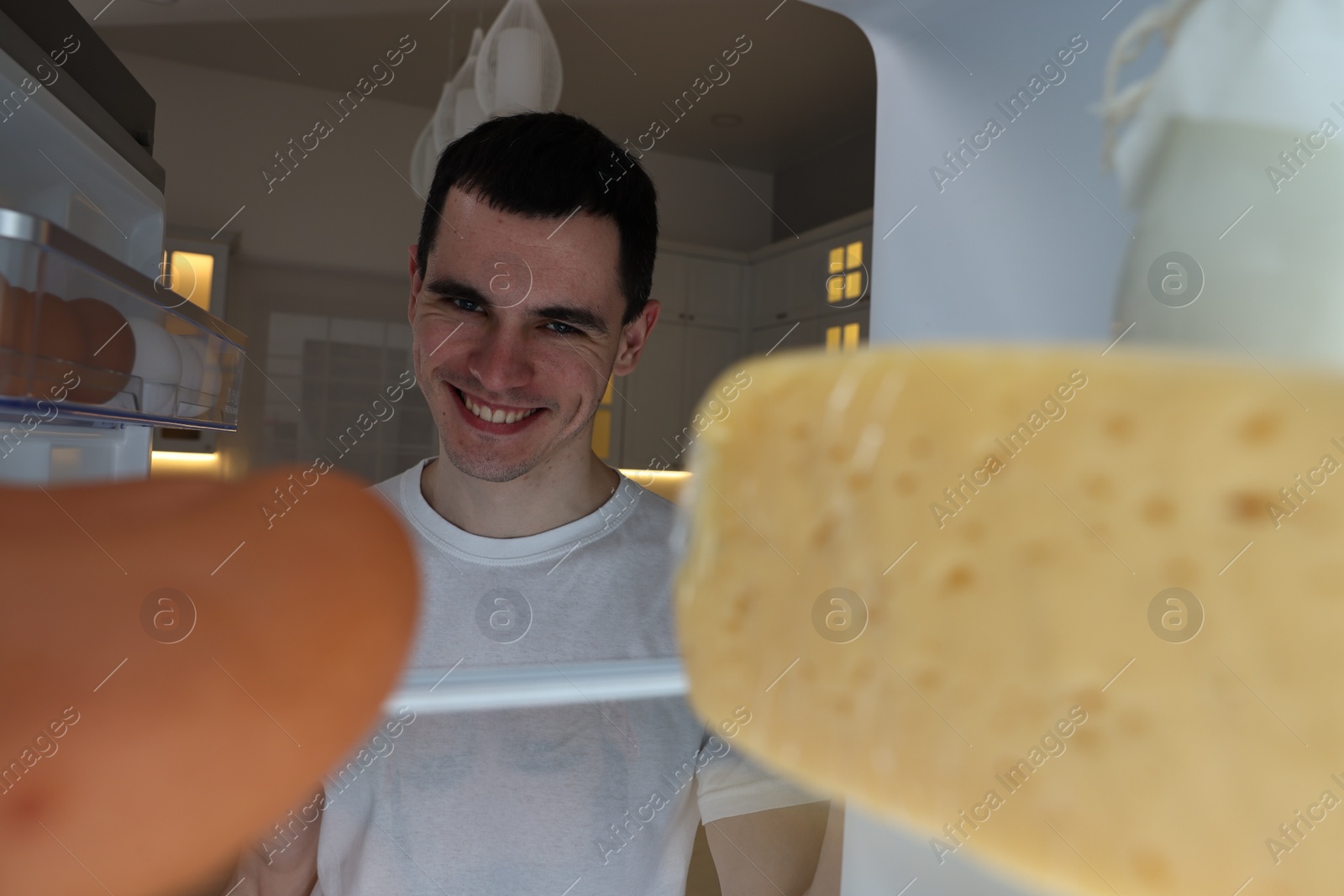 Photo of Happy man near refrigerator in kitchen at night, view from inside