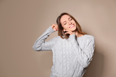 Happy young woman wearing warm sweater on beige background