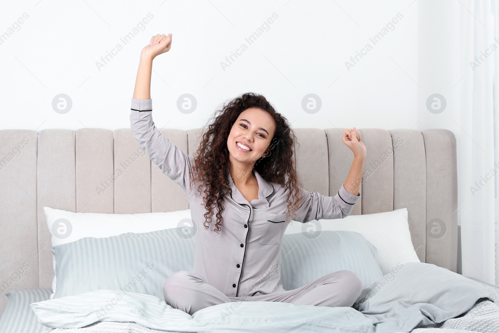 Photo of Happy beautiful African American woman stretching on bed at home