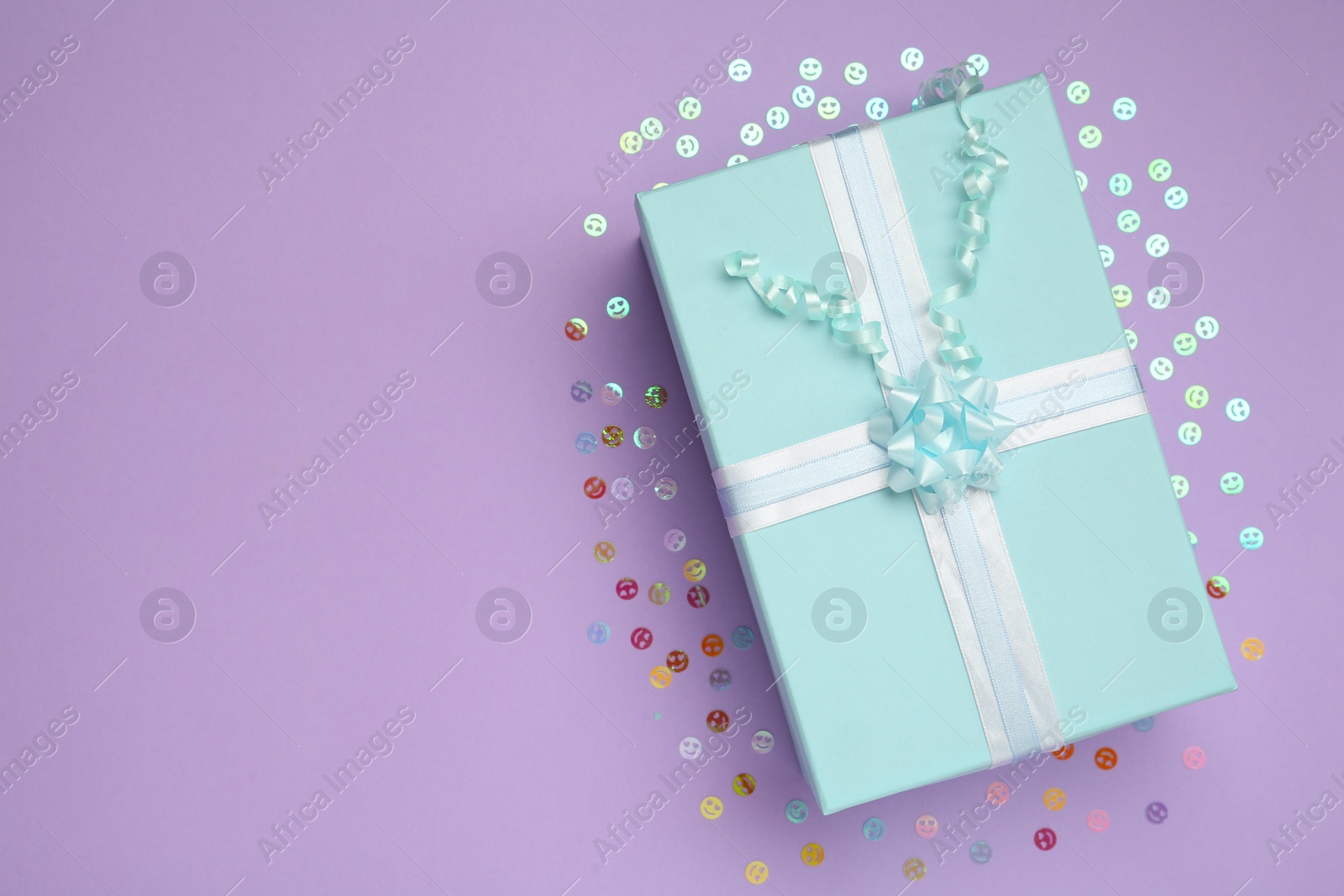 Photo of Light blue gift box and confetti on lilac background, flat lay. Space for text