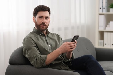 Photo of Handsome man with smartphone on sofa at home