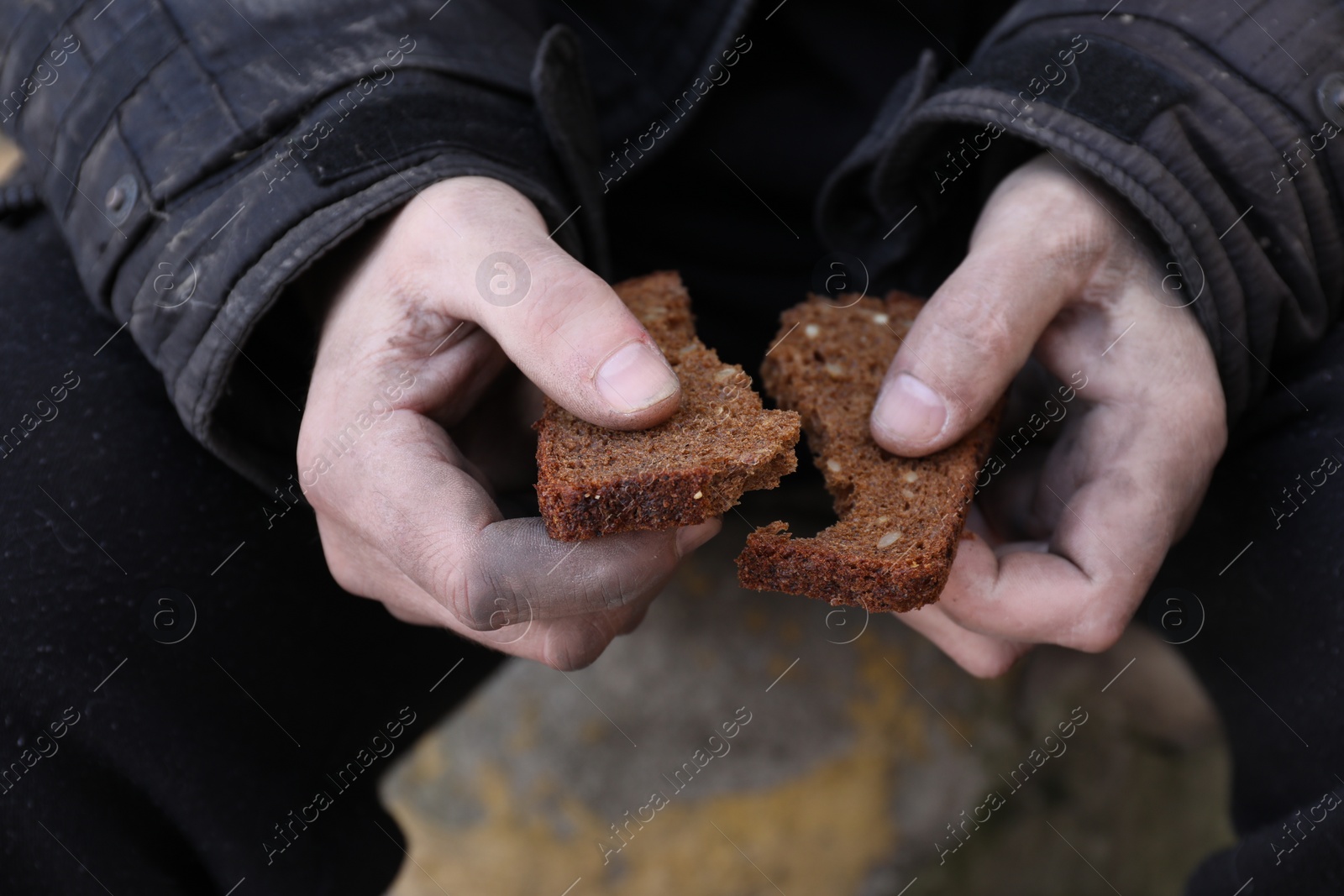 Photo of Poor homeless man holding piece of bread outdoors, closeup