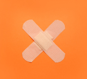 Sticking plasters on orange background, top view