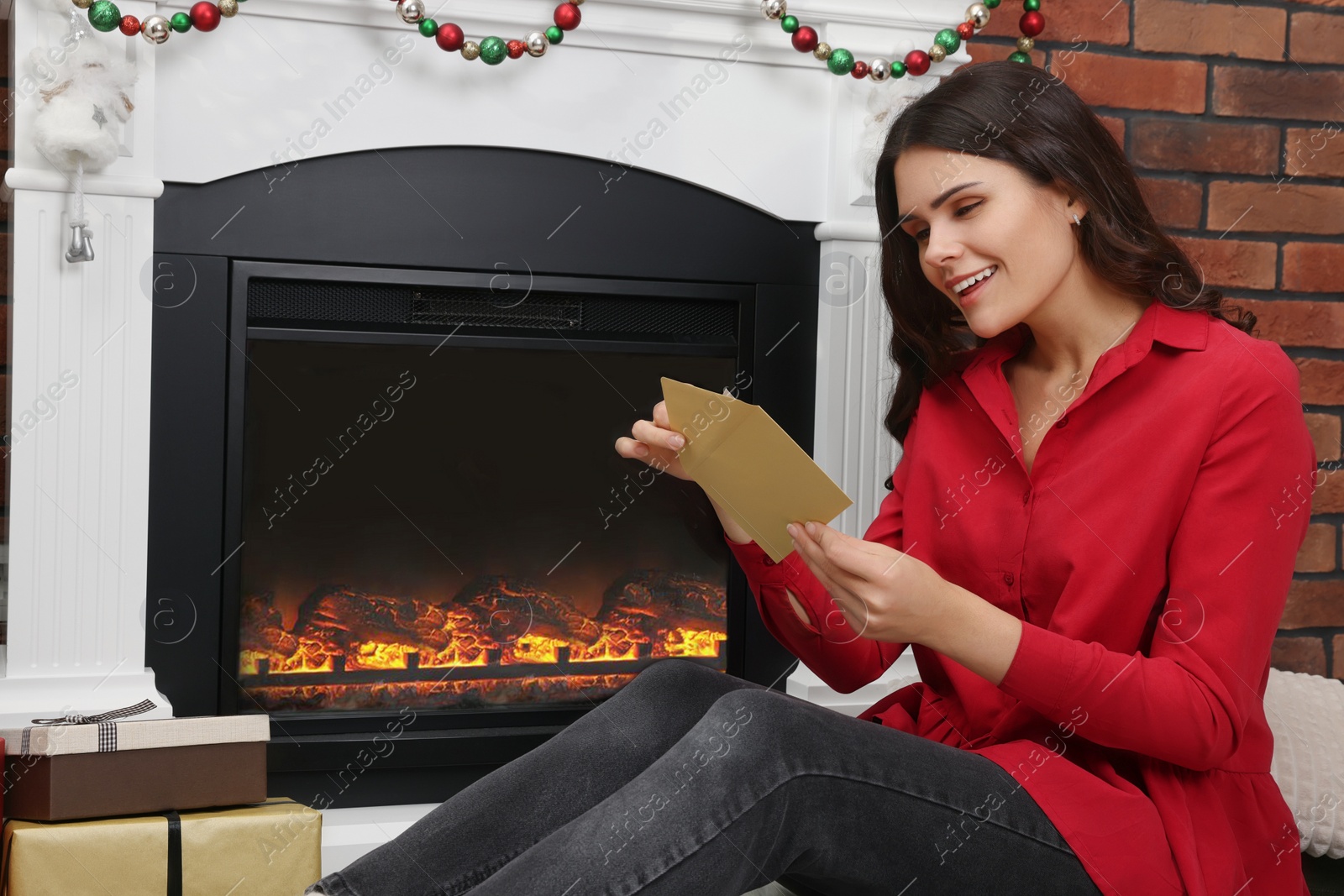 Photo of Young woman with greeting card sitting near fireplace indoors