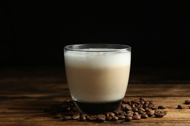 Photo of Delicious latte macchiato and coffee beans on wooden table against black background
