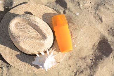 Photo of Stylish straw hat, sea shell and sunscreen on sandy beach, top view