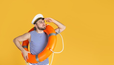 Young sailor with ring buoy on yellow background