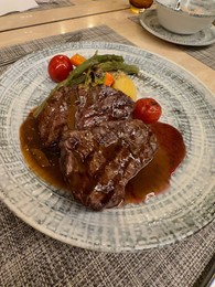 Photo of Delicious grilled beef steaks with sauce and vegetables served on table, closeup