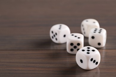 Photo of Many white game dices on wooden table, closeup. Space for text