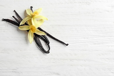 Flat lay composition with vanilla sticks and flowers on wooden background. Space for text