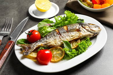 Photo of Delicious roasted fish with lemon and vegetables on dark grey table