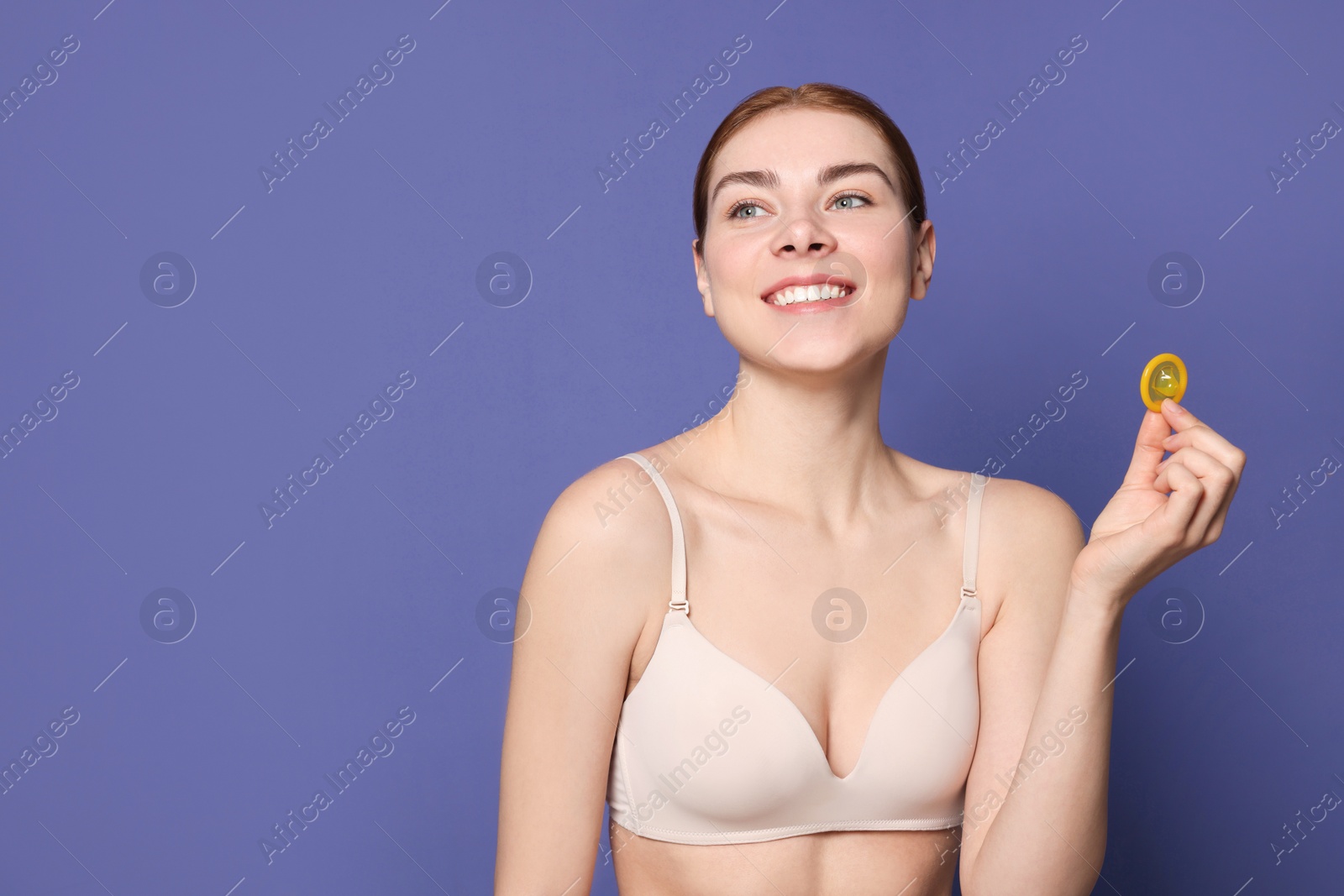 Photo of Woman in bra holding condom on purple background, space for text. Safe sex