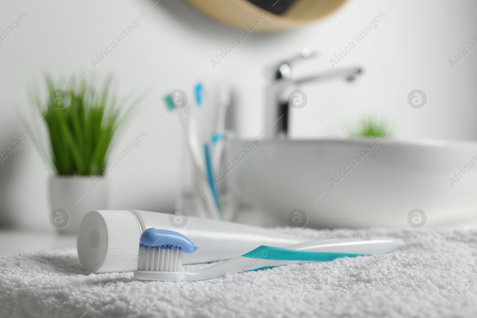 Photo of Plastic toothbrush with paste and tube on white towel in bathroom, closeup. Space for text