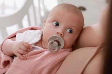 Photo of Mother holding her cute little baby with pacifier at home, closeup