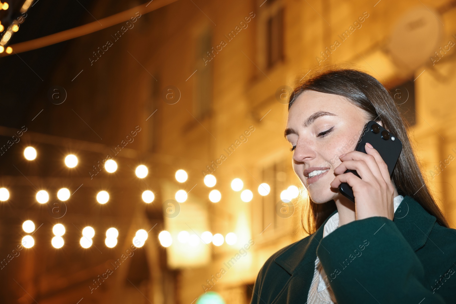 Photo of Smiling woman talking by smartphone on night city street. Space for text