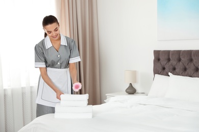 Photo of Chambermaid putting flower on fresh towels in hotel room. Space for text
