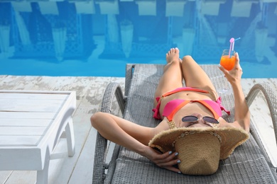 Young woman in stylish pink bikini with cocktail near swimming pool