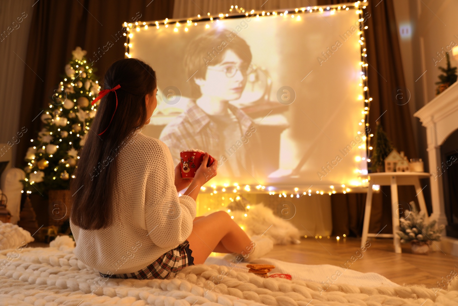 Photo of MYKOLAIV, UKRAINE - DECEMBER 24, 2020: Woman watching Harry Potter and Philosopher's Stone movie via video projector in room. Cozy winter holidays atmosphere