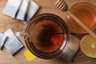 Tea bag in glass cup, honey and lemon on wooden table, top view