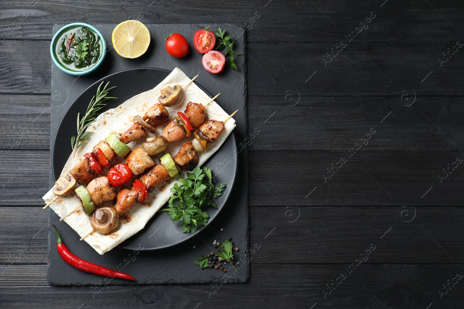 Photo of Delicious shish kebabs with vegetables served on black wooden table, top view. Space for text