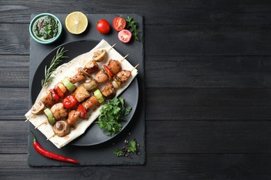 Delicious shish kebabs with vegetables served on black wooden table, top view. Space for text