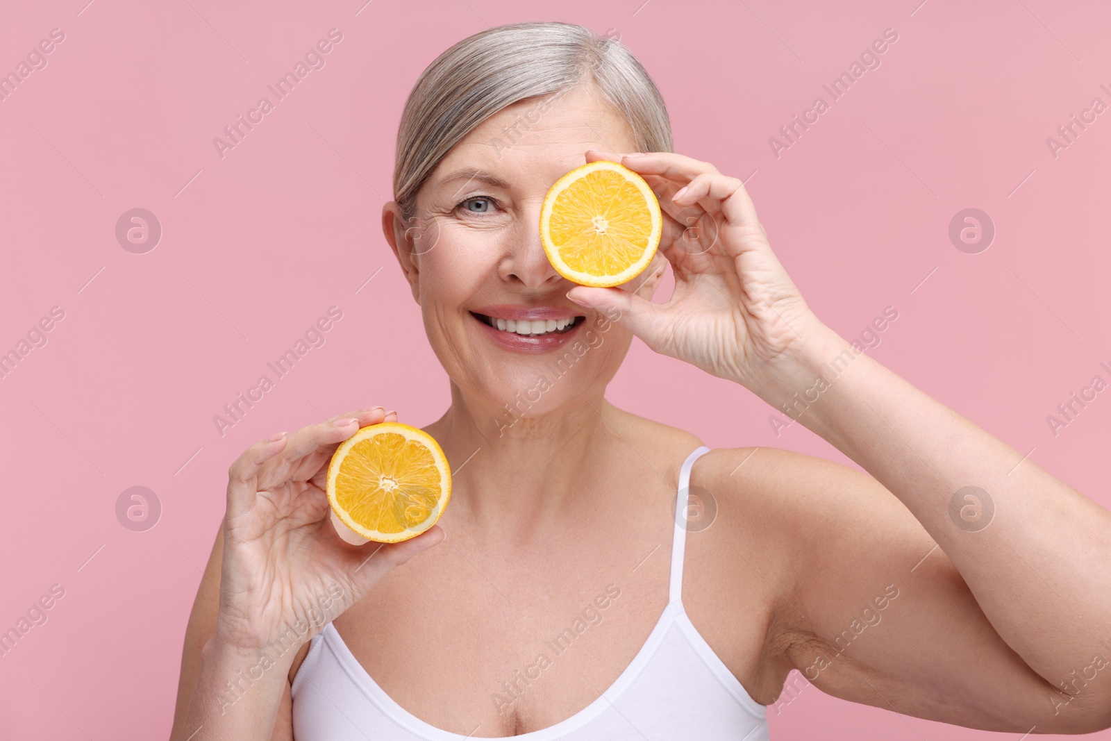 Photo of Beautiful woman with halves of orange rich in vitamin C on pink background