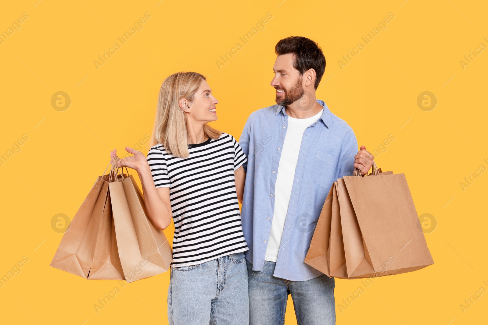 Photo of Family shopping. Happy couple with paper bags on orange background