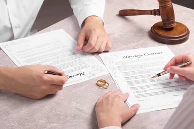 Man and woman signing marriage contract at light grey table, closeup