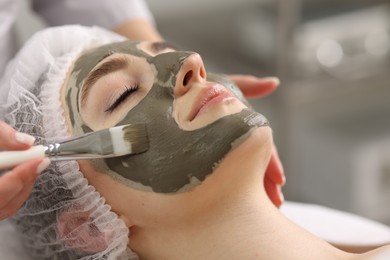 Photo of Cosmetologist applying mask on woman's face in clinic, closeup