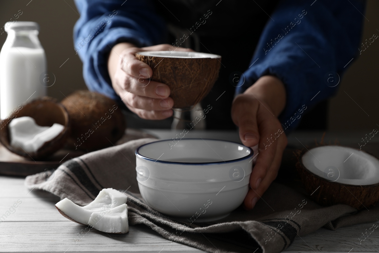 Photo of Woman holding nut with coconut milk at white wooden table, closeup