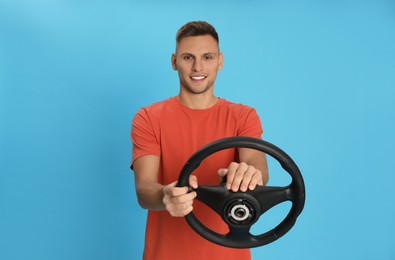 Photo of Happy man with steering wheel on light blue background. Space for text