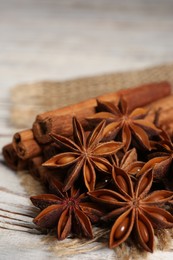 Many aromatic anise stars and cinnamon sticks on white wooden table, closeup
