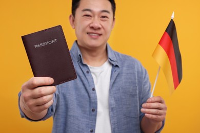 Photo of Immigration. Happy man with passport and flag of Germany on orange background, selective focus