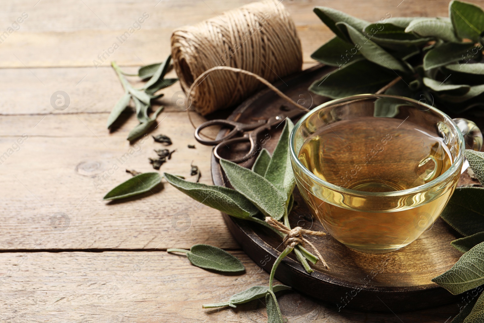 Photo of Cup of sage tea and green leaves on wooden table. Space for text