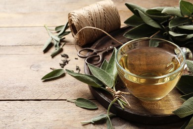 Photo of Cup of sage tea and green leaves on wooden table. Space for text