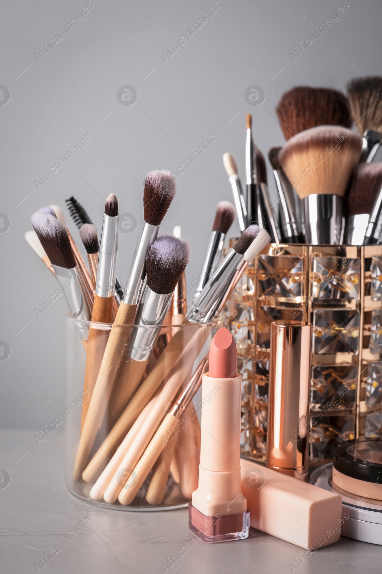 Photo of Set of professional brushes and makeup products on table against grey background