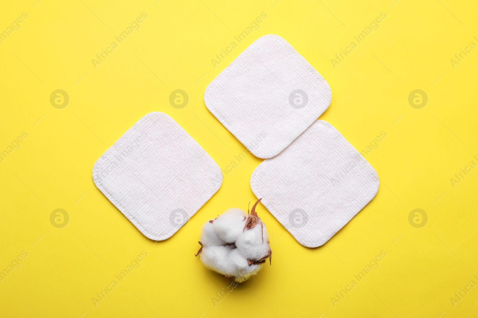 Photo of Soft clean cotton pads and flower on yellow background, flat lay