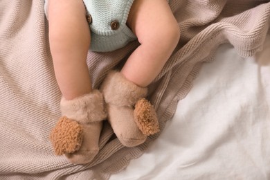Cute newborn baby in knitted booties lying on bed, top view