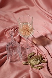 Photo of Glass of tasty alcoholic drink, empty one and golden decorative turtle on color fabric