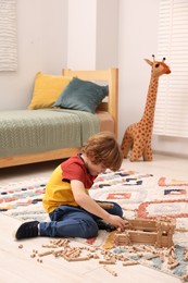 Photo of Little boy playing with wooden construction set on carpet in room. Child's toy