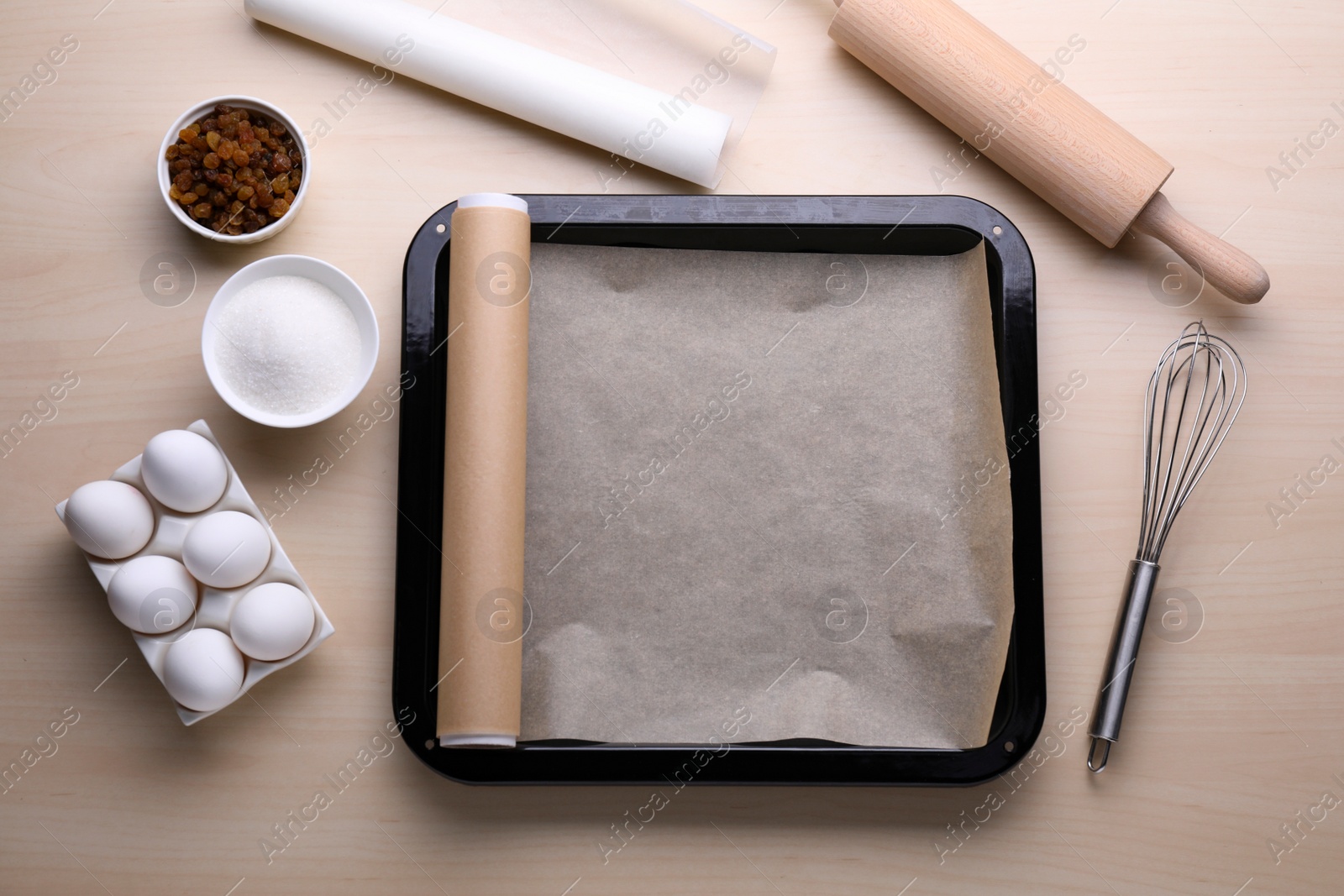 Photo of Baking pan with parchment paper, different ingredients and kitchen tools on wooden table, flat lay